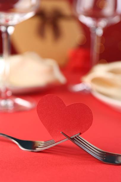 Joined forks with paper heart on red table, closeup. Romantic dinner