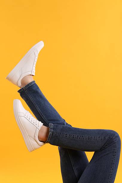 Man wearing stylish white sneakers on yellow background, closeup