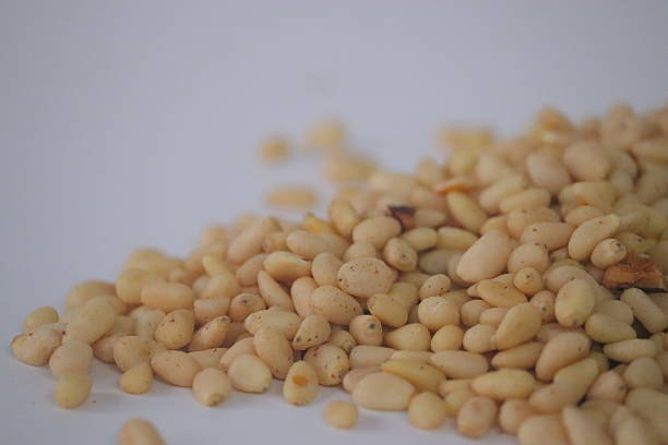 Pine nuts, also known as pine kernels, presented in a loose pile, featuring shelled seeds on a clean surface. Close-up food image highlighting smooth texture, commonly used in Mediterranean cuisine for pesto and baking