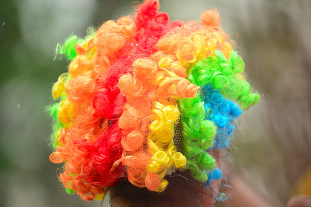 Close-up view of a vibrant, curly clown wig in bright rainbow colors, photographed from behind with no visible face. The playful texture and bold colors create a fun and energetic mood. Ideal for concepts related to carnival, circus, entertainment, humor, celebration, childhood, creativity, costume design, and festive events.