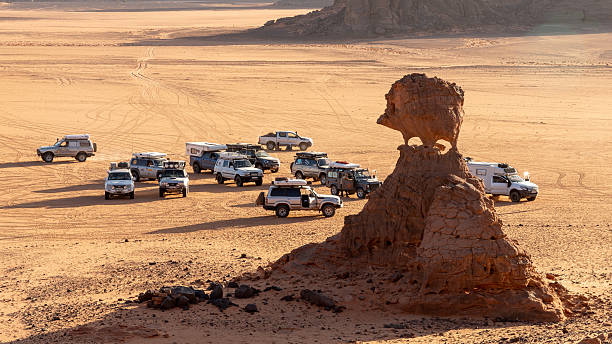 A group of 4x4 camper vans are gathered in front of the famous rock formation known as Hérisson in the Tadrat Rouge, in the heart of the Algerian Sahara