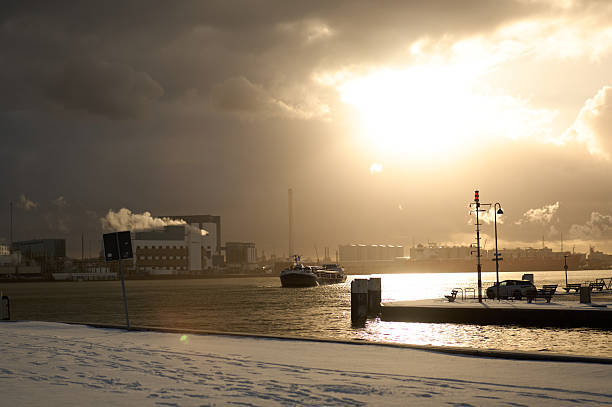 Tugboat navigating through a snowy port under dramatic cloudy skies and golden sunset light