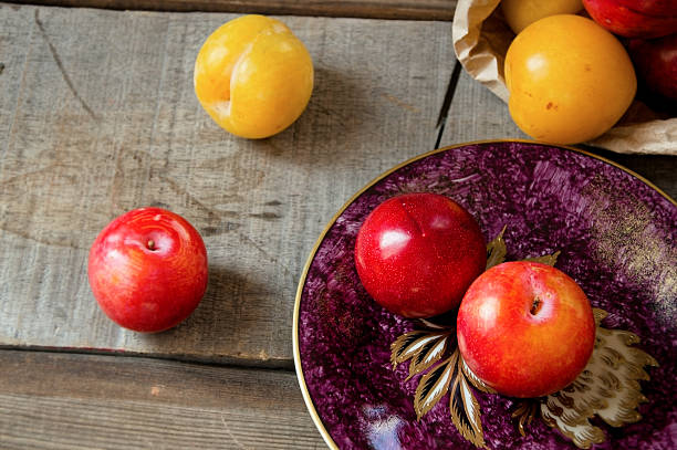 A mix of yellow and red plums on a purple antique plate and rustic tabletop, with open copy space for text on the upper left side.