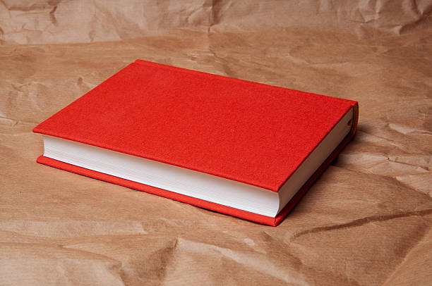A simple, elegant red book with crisp white pages lies on crumpled brown paper, creating a minimalist composition