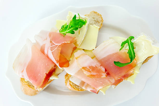 Two open faced sandwiches with ham and egg topped with mayonnaise, potato salad, cucumber, pepper and  decorated with arugula on plate. White background, selective focus, shallow DOF. Clipping path included.