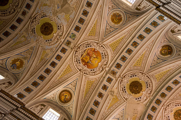 Intricately decorated vaulted ceiling with detailed frescoes and geometric patterns inside the Cattedrale dell'Immacolata Concezione in Bosa, Sardinia. Warm natural light highlights the elaborate stucco and classical motifs.