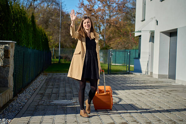 istock Woman pulling suitcase and waving hand near modern building 2255967615