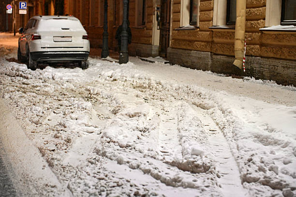 White car headlight and front fender blanketed in fresh snow, close-up showing icy buildup and frosted glass, conveying harsh winter conditions and travel risk