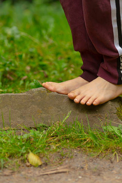 bare feet on stone edge, white child balancing in sweatpants, mossy rock and green grass, closeup focus on toes, tactile nature moment, tranquil outdoor exploration