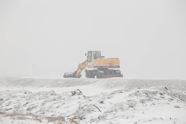 Earth mover on flattening layer of gravel building new road in winter