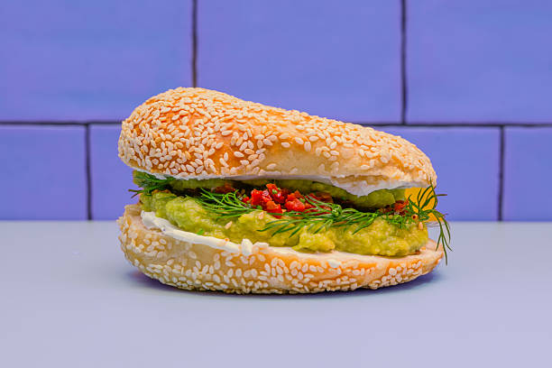 A perfectly toasted rye bagel, covered with an even layer of cream cheese and translucent flakes of cured salmon, presented with a sprig of dill on a white plate