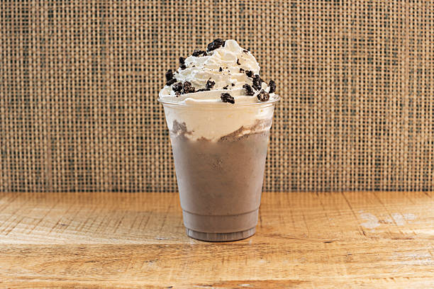 A thick, cold chocolate milkshake served in a tall glass, topped with a generous dollop of whipped cream that gently spills over the sides.