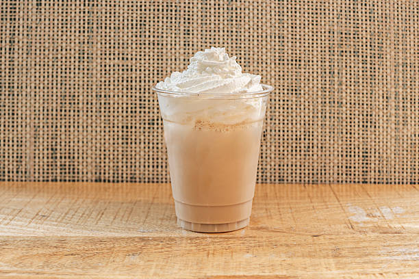 Light brown milk chocolate milkshake, characterized by its smooth, homogeneous texture, topped with a dense foam of freshly whipped cream with a straw inserted in the center.