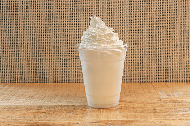 Close-up of the texture and contrast between a thick chocolate milkshake and the light whipped cream that accompanies it, showing drops of liquid chocolate sliding down the sides of the glass.