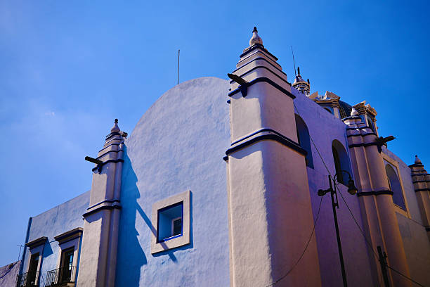 A white and blue church facade rises against a cloudless sky in strong afternoon light.