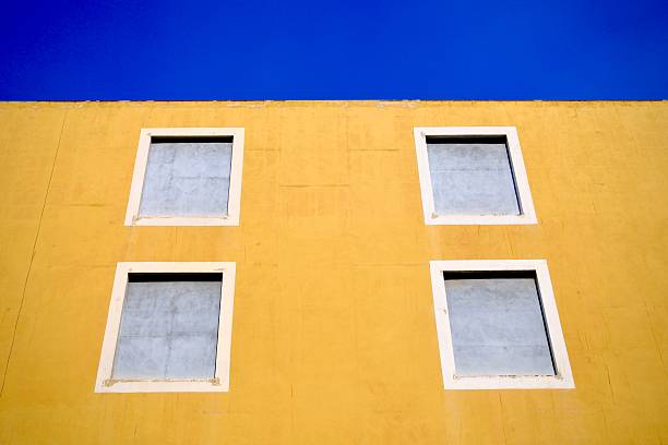 A bold yellow facade shows evenly spaced windows beneath a deep blue sky.