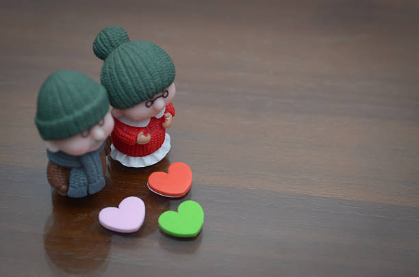 Miniature elderly couple with hearts on wooden surface, symbolizing enduring love, companionship, and affection in later life.