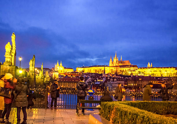 Prague,Czech Republic- December 18 2014:People sightseeing on scenic spot by Charles bridge on Vltava river bank enjoying the night blue skyline of Prague Castle and Old Town