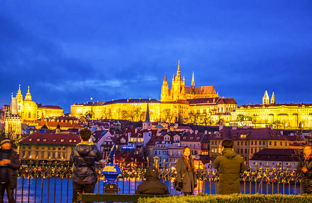 Prague,Czech Republic- December 18 2014:People sightseeing on scenic spot by Charles bridge on Vltava river bank enjoying the night blue skyline of Prague Castle and Old Town