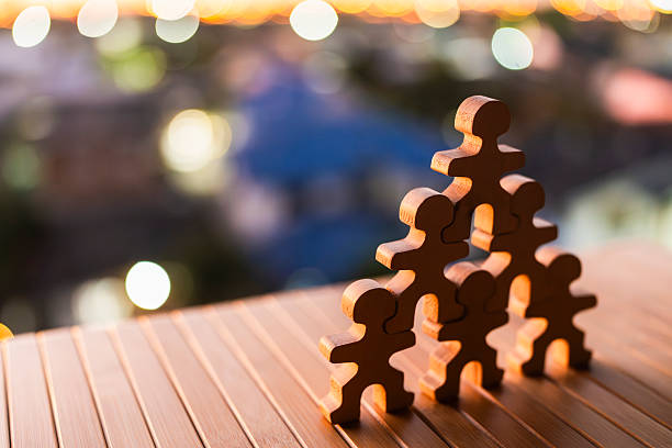 istock Wooden human figures standing in hierarchy formation on table with city bokeh background, representing business competition, industry survival, corporate structure, workforce pressure and economic struggle concept. 2255997996