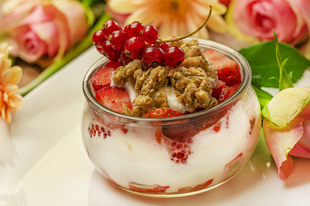Yogurt dessert with strawberries currants and granola on plate with flowers, elegant healthy breakfast presentation