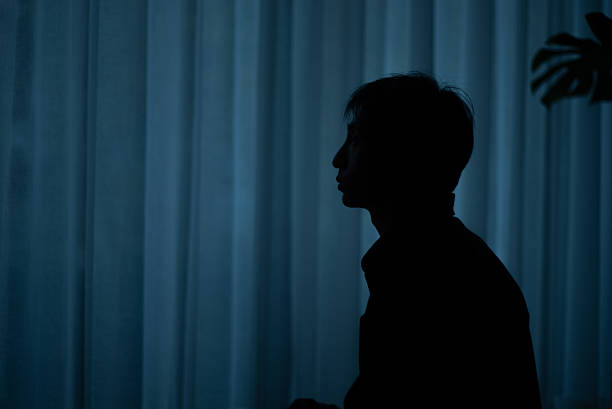 Silhouette of a lonely man sitting by a window at night feeling depressed.