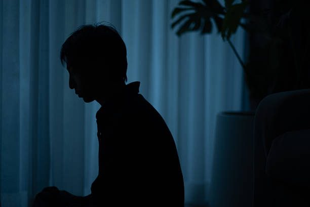 Silhouette of a lonely man sitting by a window at night feeling depressed.