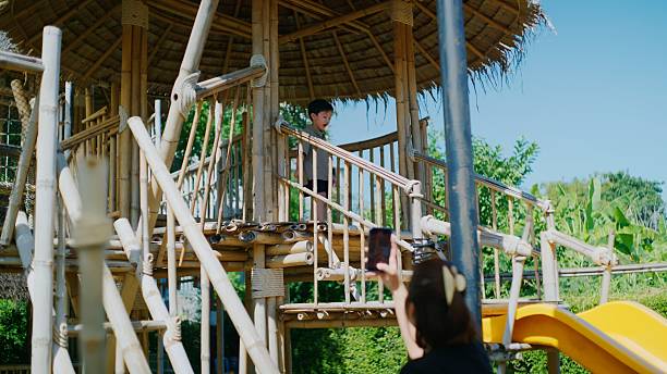 Happy and energetic Asian boy plays on a bamboo climbing structure and slide at a kids’ café, having fun and enjoying an exciting, child-friendly environment made from natural materials.
