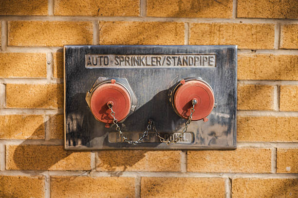 Fire department connection with dual standpipe and auto-sprinkler caps mounted on a brick wall in bright sunlight. High quality photo