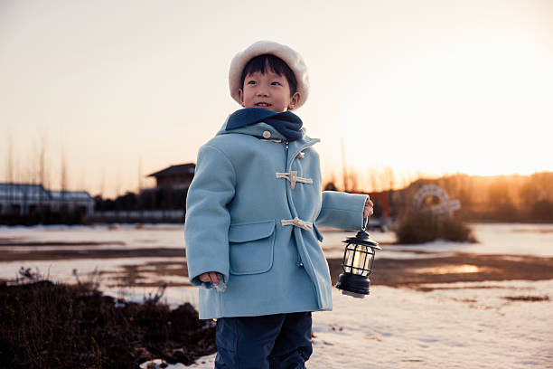 This is an Asian boy, about 5 years old. He is wearing a blue winter coat and playing outdoors in the snow.