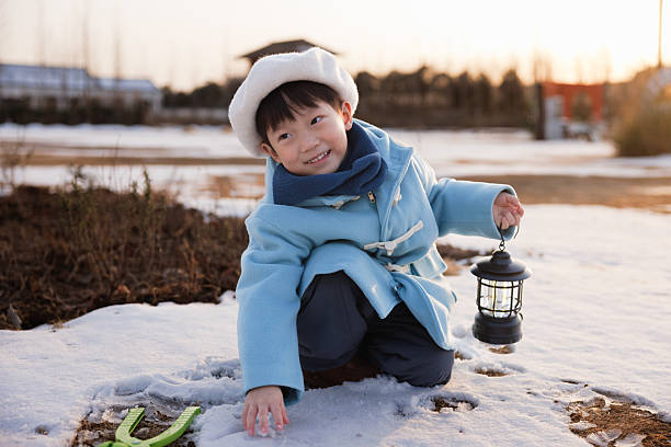 This is an Asian boy, about 5 years old. He is wearing a blue winter coat and playing outdoors in the snow.