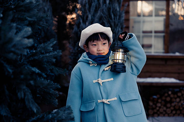 This is a Chinese little boy, 5 years old. In the winter outdoors, he stood in front of a house decorated in Christmas style, holding a lantern and playing.