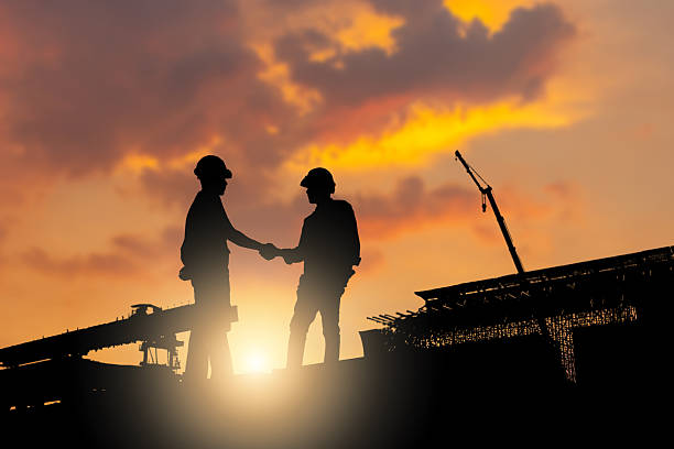 istock Silhouette of construction workers shaking hands at industrial site during sunset, Business partnership agreement between engineers at infrastructure construction site, Teamwork and success concepts 2256006697