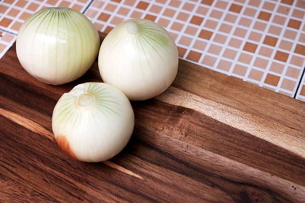 Three of raw peeled onion on wooden cutting board. Preparing fresh vegetable ingredients for a homemade meal. Slicing food for a onion ring.