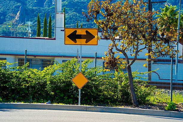 A yellow traffic sign with black arrows pointing in opposite directions, symbolizing a decision point or diverging paths