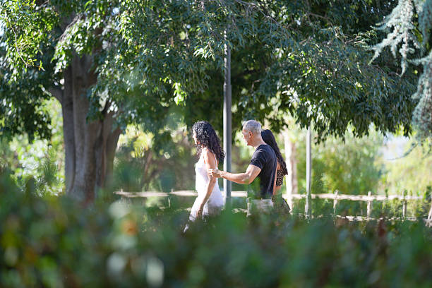A man and a woman are walking in a park. The man is holding the woman's hand