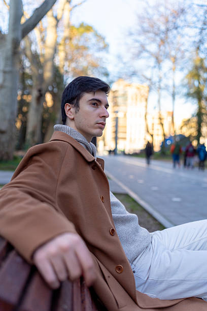 istock Young man relaxing on park bench in city after work 2256014873