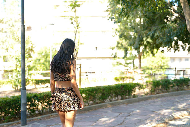 A woman in a leopard print skirt walks down a sidewalk. The image has a casual, relaxed mood, as the woman is dressed in a comfortable outfit and he is enjoying her walk