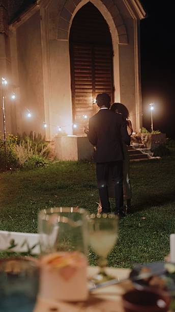 The bride and groom are dancing a slow dance near an old chapel at night