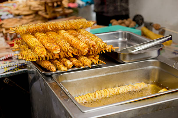 Golden fried spiral-cut potatoes displayed on wooden sticks in steel tray above oil fryer at street food market festival booth
