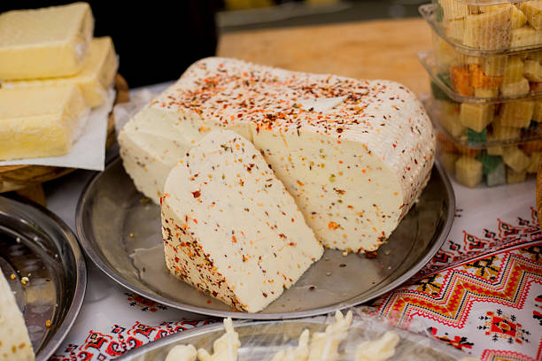 Sliced white cheese generously coated with red paprika spices arranged on metal plate over traditional embroidered textile with ethnic patterns