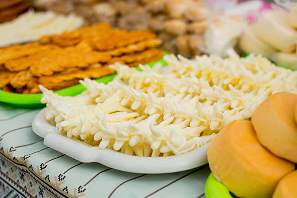 White plate filled with freshly grated cheese alongside sliced yellow hard cheese and various dairy products on embroidered table setting