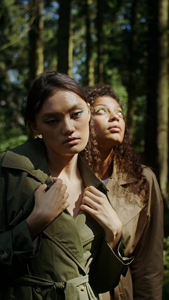 Two women of different nationalities pose standing in the forest, vertical