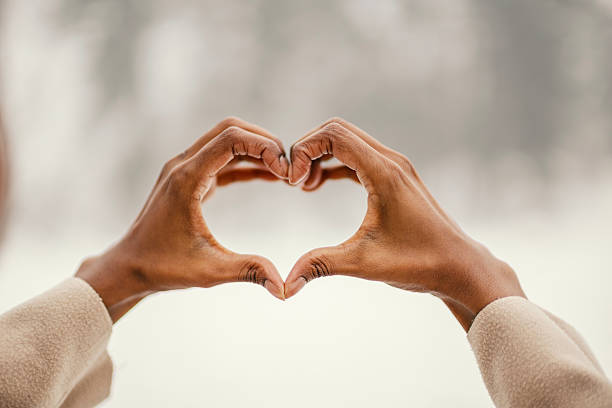 Human hands forming a heart gesture against a soft blurred background, symbolizing love, kindness, unity, care, friendship and positive connection in a warm outdoor light
