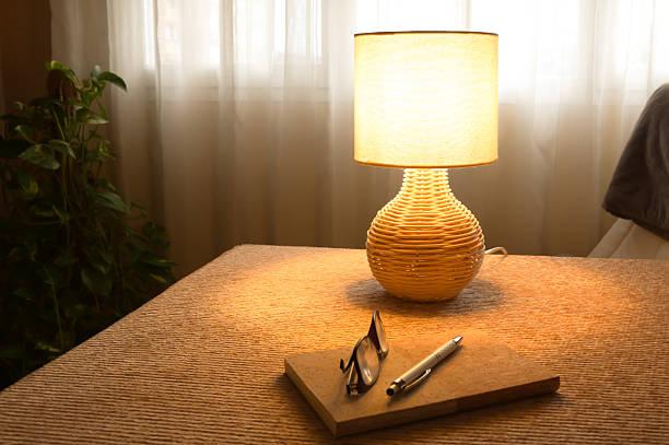Woven rattan table lamp casts warm, energy-saving light over a notebook, pen and glasses on a cozy desk, evoking sustainable home living, study and quiet evening reflection