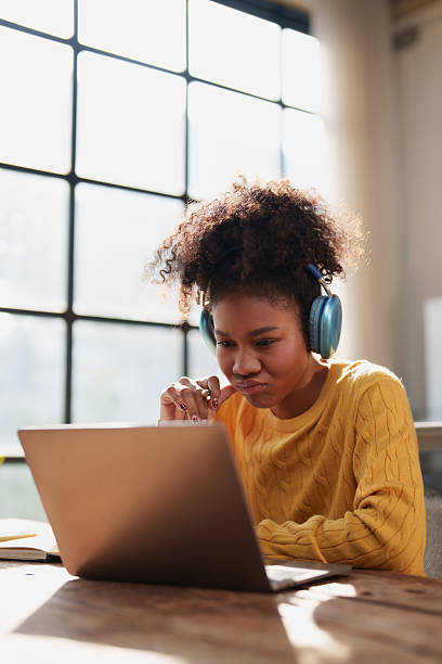 istock Young female student with afro hair deeply concentrating while studying online, using headphones and a laptop, suggesting remote education or focused work 2256026950
