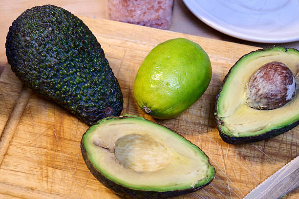 An assortment of fresh Guatemalan fruits including a ripe avocado surrounded by small green limes, isolated on a white background. This vibrant composition highlights tropical produce ideal for culinary, nutrition, and agricultural themes in commercial use.