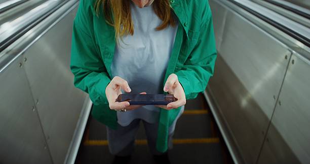 A woman plays an online game on a smartphone while going up the escalator in the subway