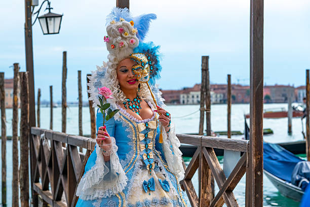 Venice, Italy - March 3, 2014: The photo was taken during the famous Venice carnival in front the San Zaccaria church on Campo San Zaccaria. We can see attractive masked young woman who wearing traditional carnival costume with rose shape. Venice, Italy.