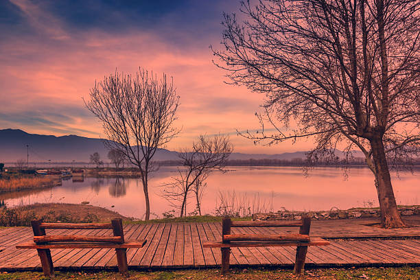 Kerkini, Northern Greece  Wooden benches overlook the calm lake at sunset, framed by leafless trees and warm reflections.
